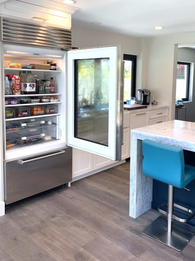 Modern kitchen with an open fridge next to a blue bar stool at the island.