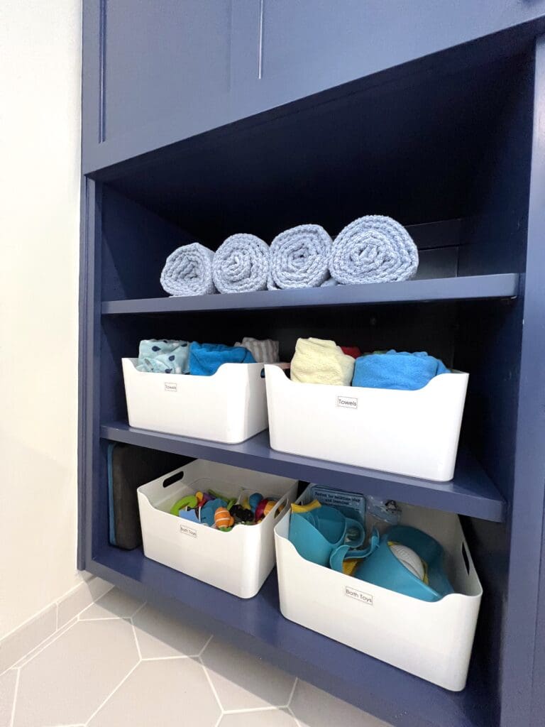Organized shelf with rolled towels and plastic bins containing toiletries.