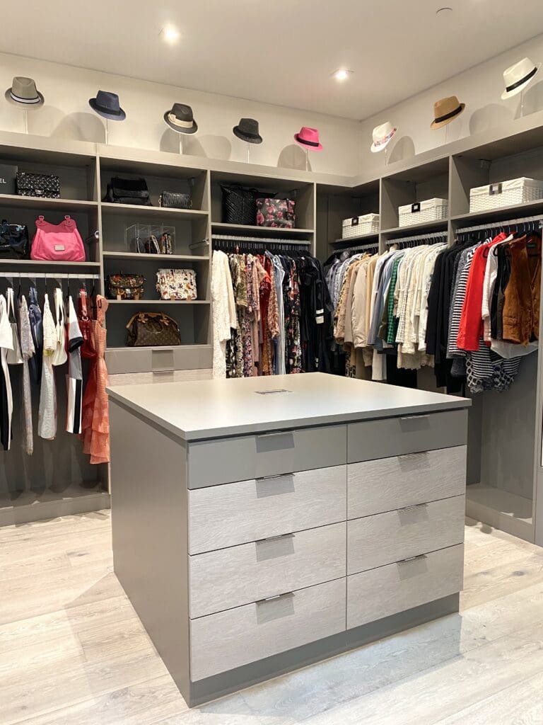 Modern walk-in closet with organized clothes and a central island with drawers.