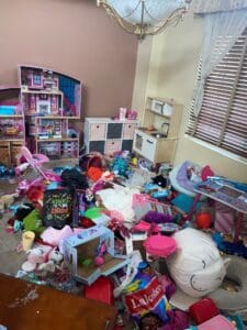 Playroom before decluttering, with toys, dolls and bins piled across the floor