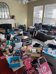 Family room before decluttering, with toys, boxes and bags covering the floor around a leather sectional