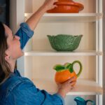 A Woman Taking a Red Ceramic Bowl from a Shelf Copy