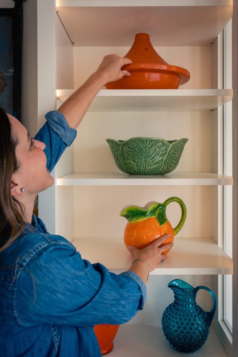 Organizer setting an orange ceramic piece on an open shelf with green and teal pottery