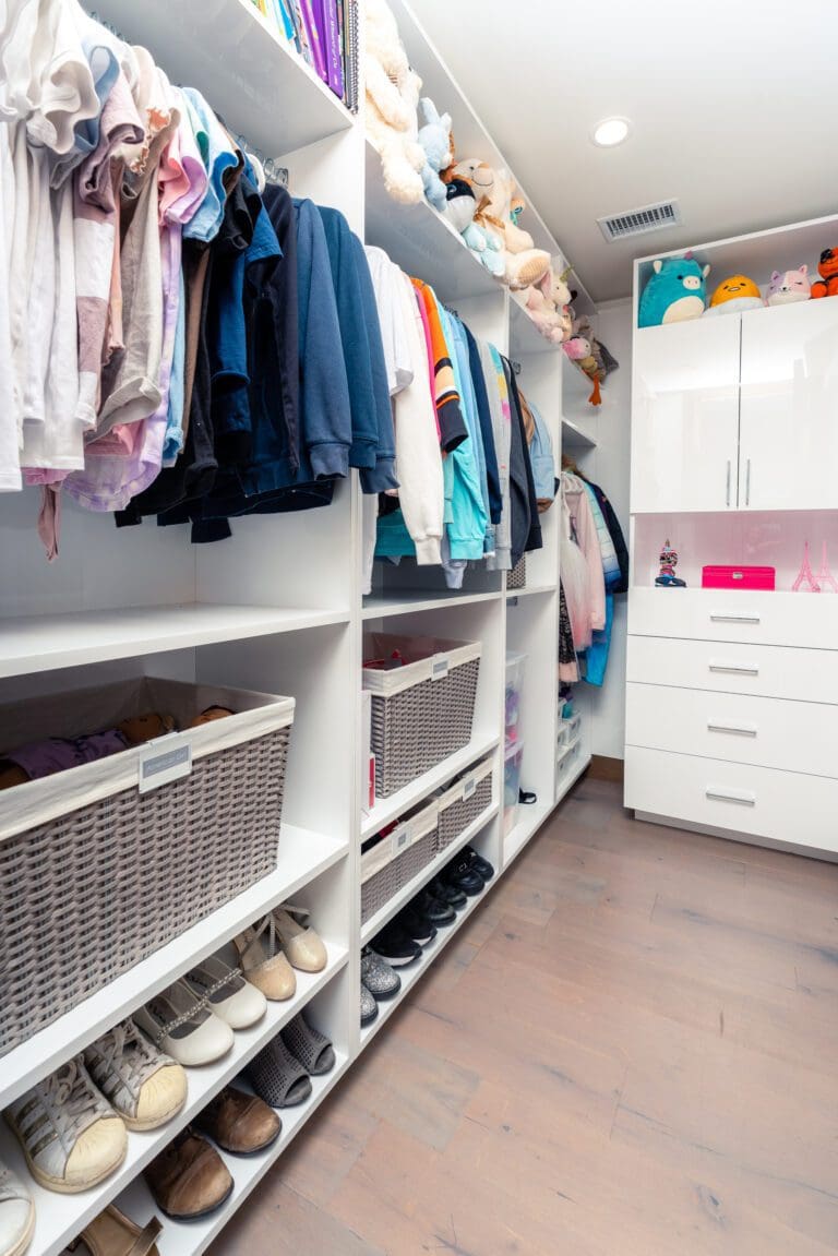 White closet with hanging clothes, woven baskets and shoe shelves