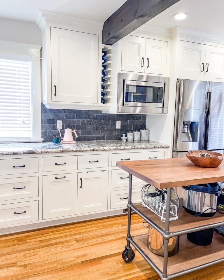 White kitchen with a gray tile backsplash, clear counters and a butcher block island cart