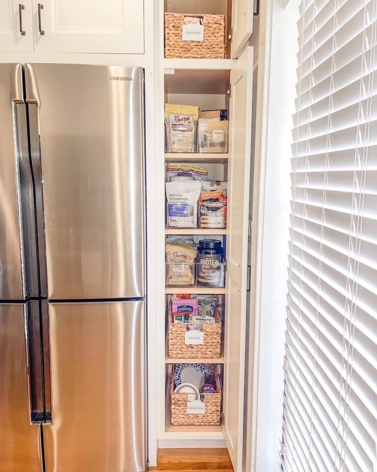 Narrow pantry cabinet beside a stainless fridge with labeled woven baskets on every shelf