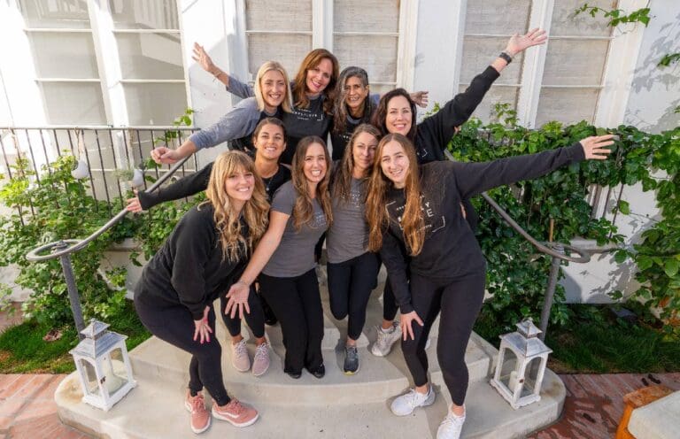 Group of seven smiling women posing cheerfully outdoors.