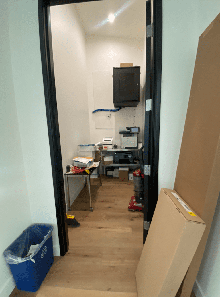 Office supply room before organizing, with a cluttered table and boxes by the door