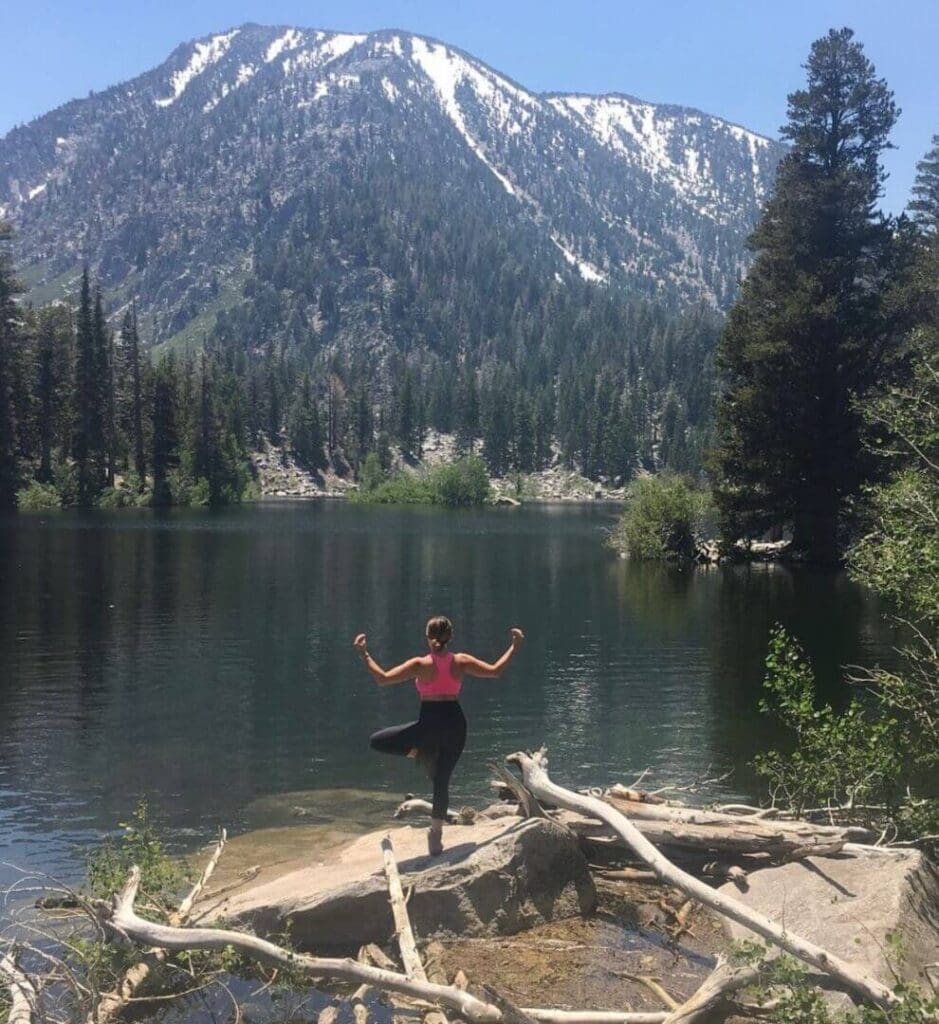 Person doing yoga by a serene lake with snow-capped mountains.