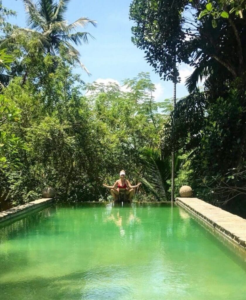 Person relaxing in a lush green infinity pool surrounded by tropical trees.