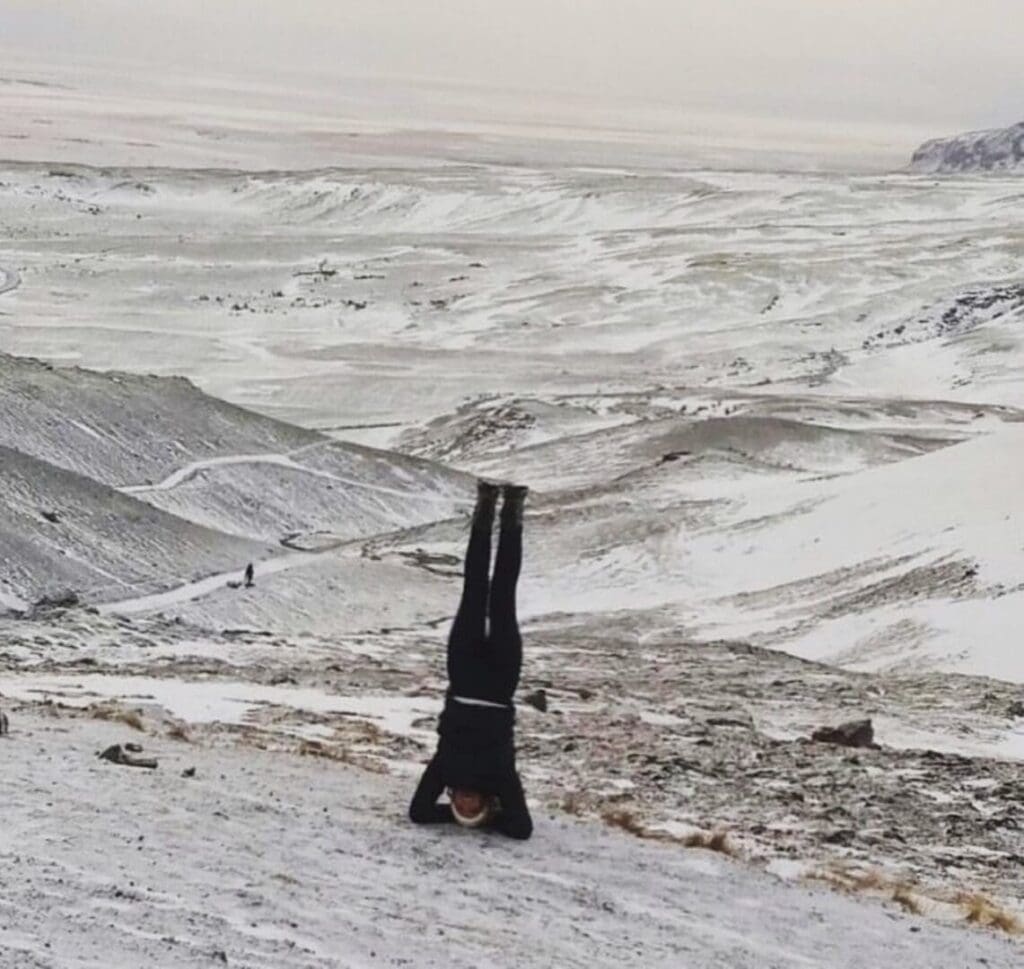 Person doing a handstand on a snowy hill with a vast snowy landscape.