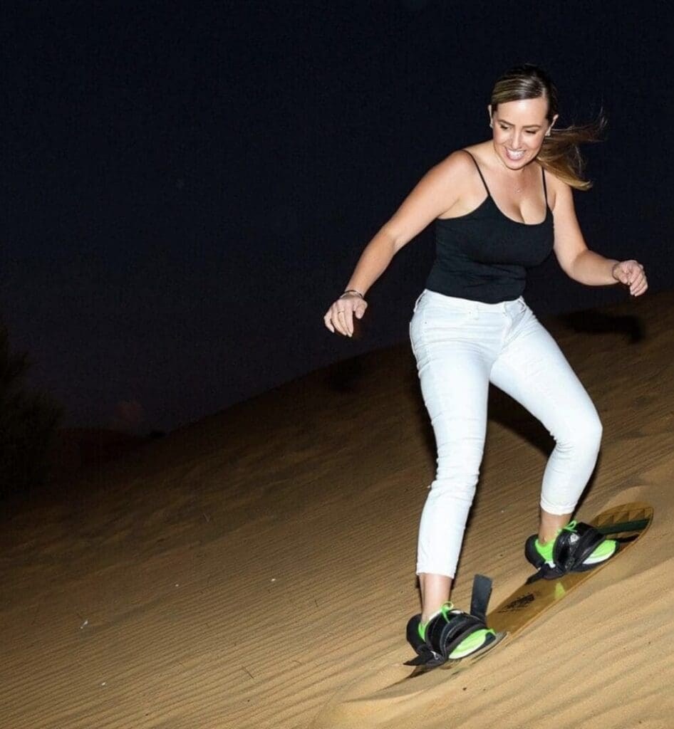 A woman sandboarding at night on a dune.