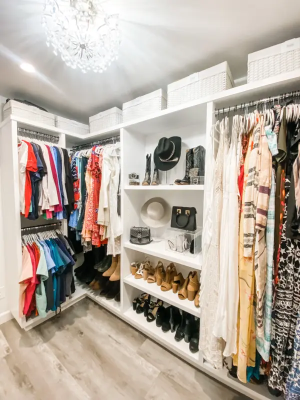 Bright walk-in closet with chandelier, white bins, hats, boots and handbags organized by Simply Luxe on HGTV's Christina on the Coast