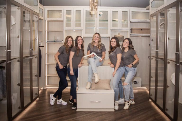 A group of five women smiling in a cozy, modern living room.