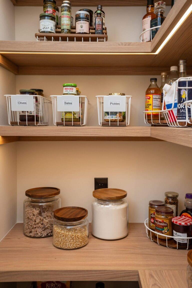 Walk-in pantry with light wood shelves, labeled wire baskets and glass jars of dry goods