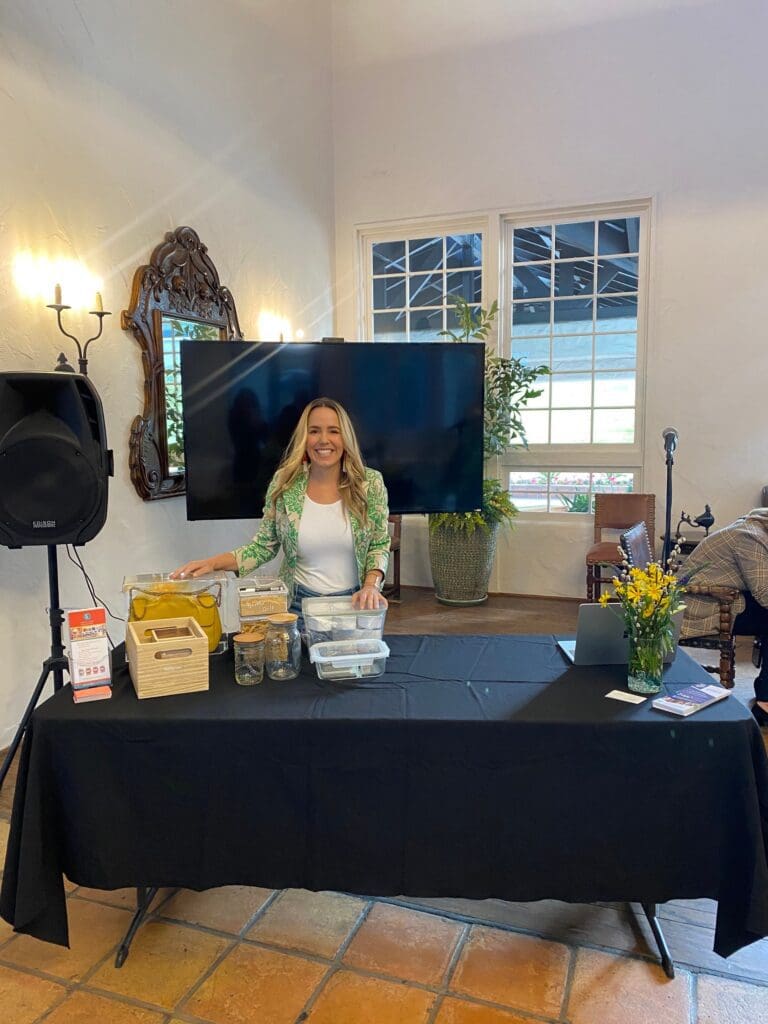 Woman standing behind a table, smiling indoors.
