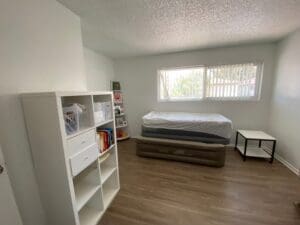 Same guest room after unpacking, boxes cleared, with a white bookshelf set up and open floor