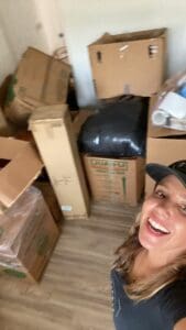 Ryen of Simply Luxe smiling among stacked moving boxes during the unpack