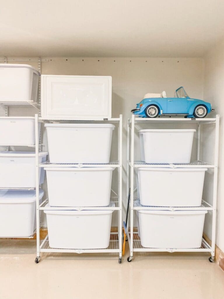 White storage bins stacked on garage shelves with a blue toy car on top