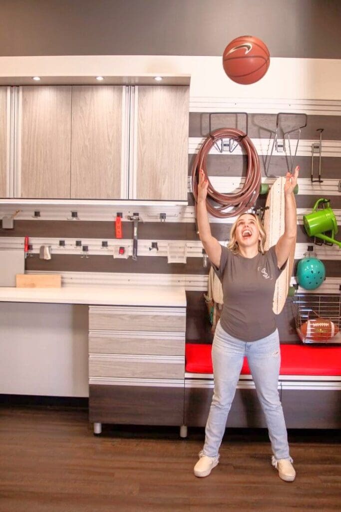 Smiling woman holding up a coiled hose in a freshly organized garage