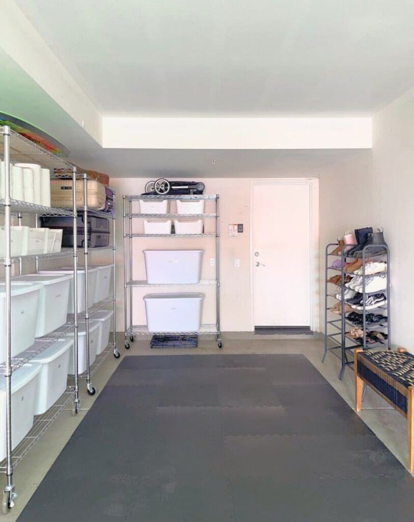 Organized garage with white shelves of storage bins and a black floor mat