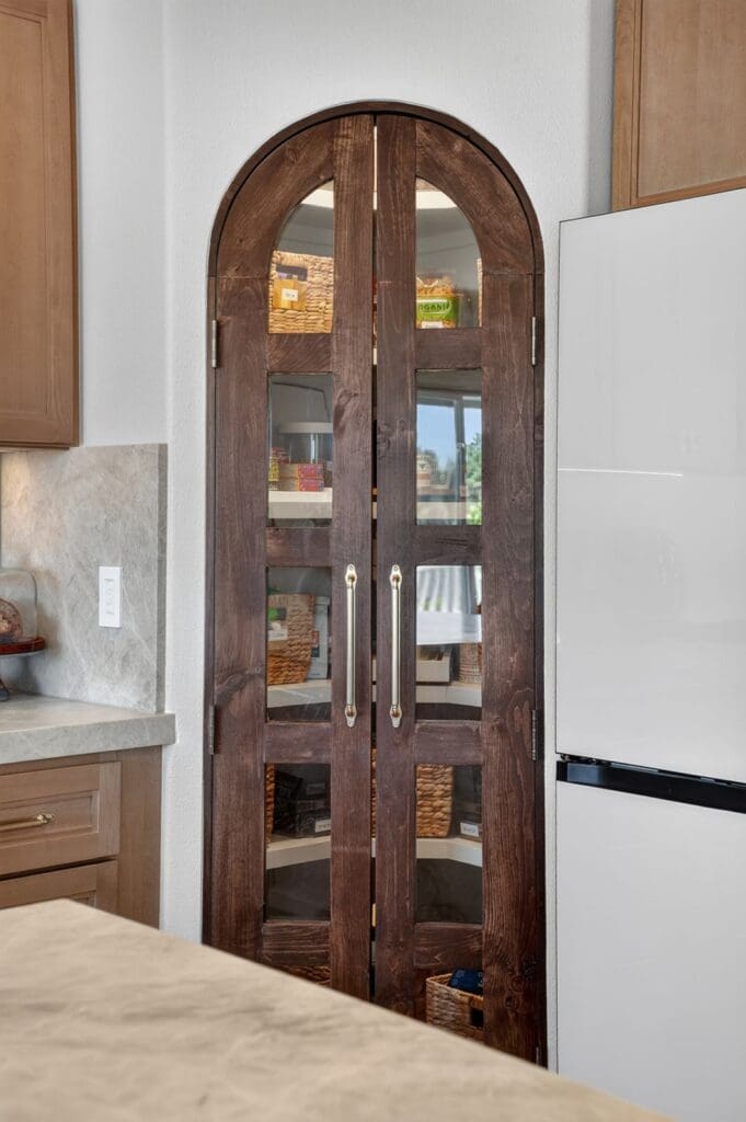 Arched glass pantry cabinet organized with baskets and canisters in a Mission Viejo kitchen