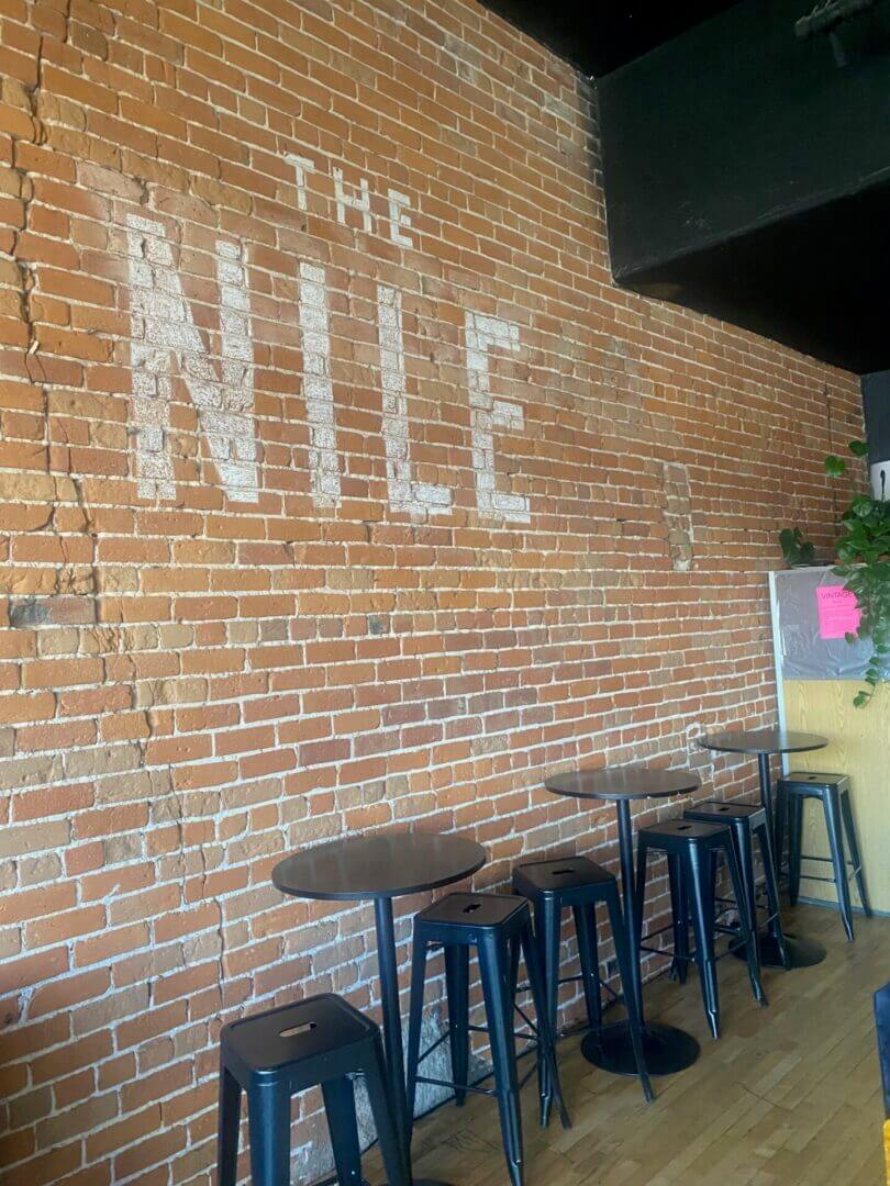 A brick wall with 'THE NILE' painted on it above wooden stools.