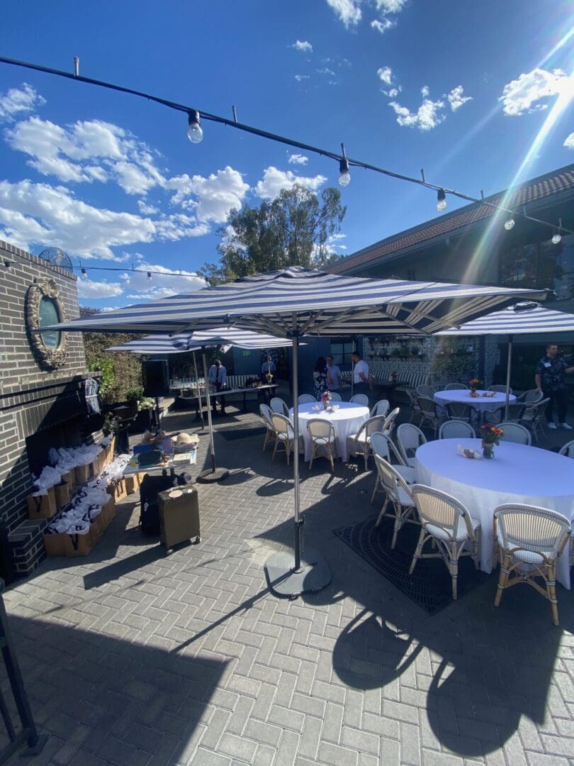 Outdoor patio with tables, chairs, and a striped awning under a bright sky.