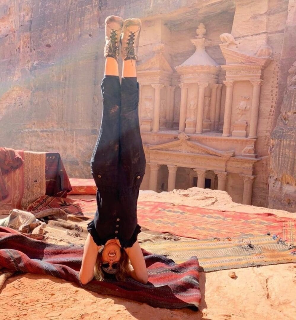 Person practicing headstand yoga with historical ruins in background.