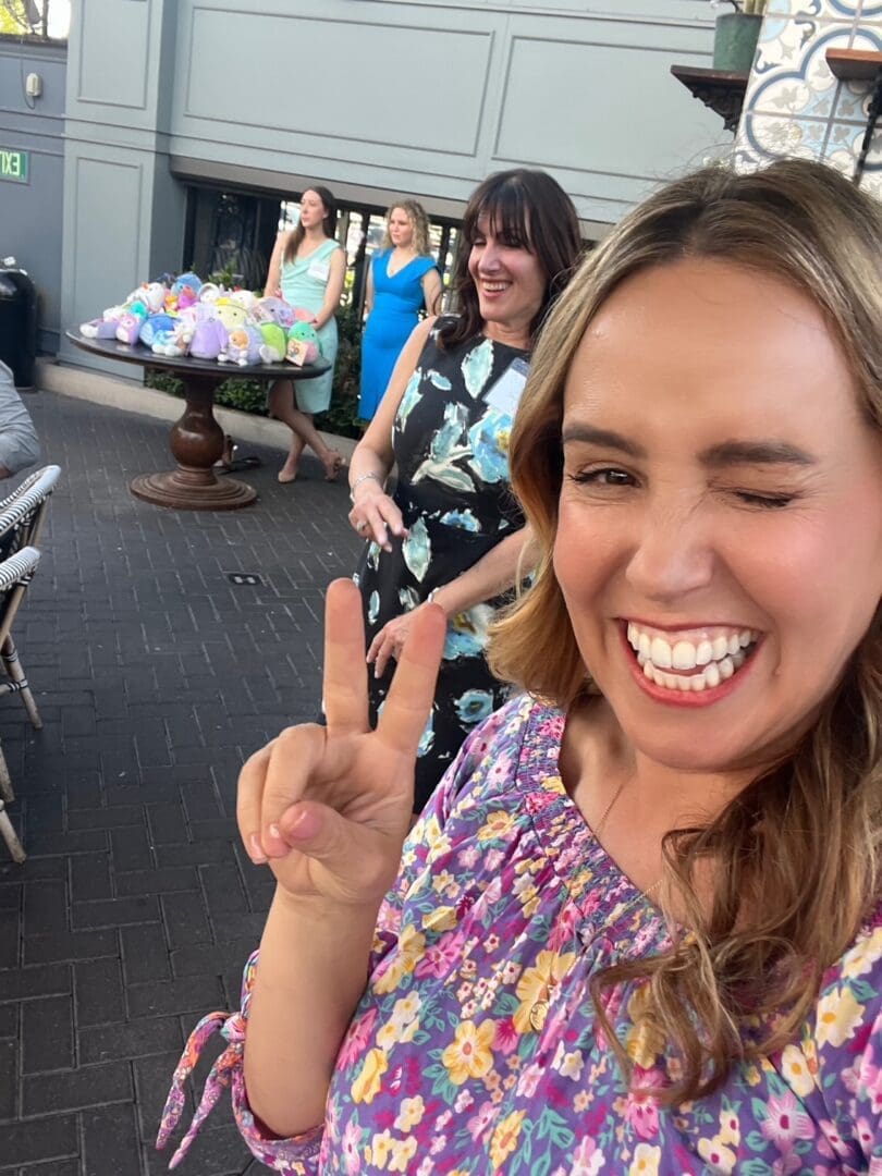 A woman smiling and winking while making a peace sign at the camera.
