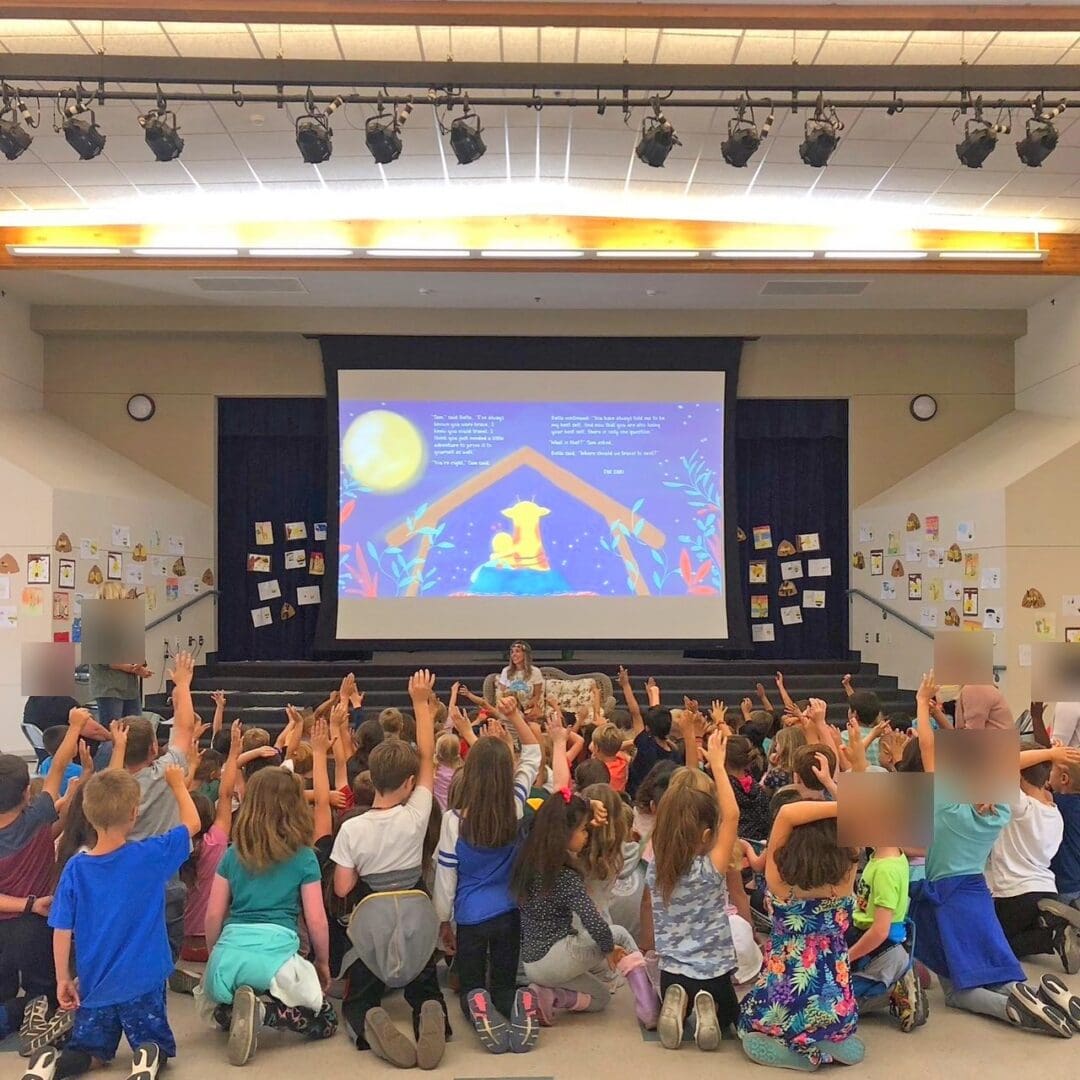 Students at Garden Road Elementary in Poway raising their hands at a Bee A Dreamer assembly, with the book projected on a large screen