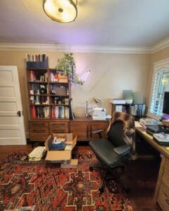 Bookshelf home office before organizing with boxes and paperwork spread across the rug, San Diego