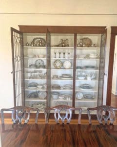 Glass china cabinet after unpacking, with silver and serving pieces arranged shelf by shelf, Orange County