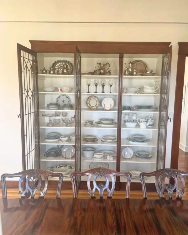 Glass china cabinet after unpacking, with silver and serving pieces arranged shelf by shelf