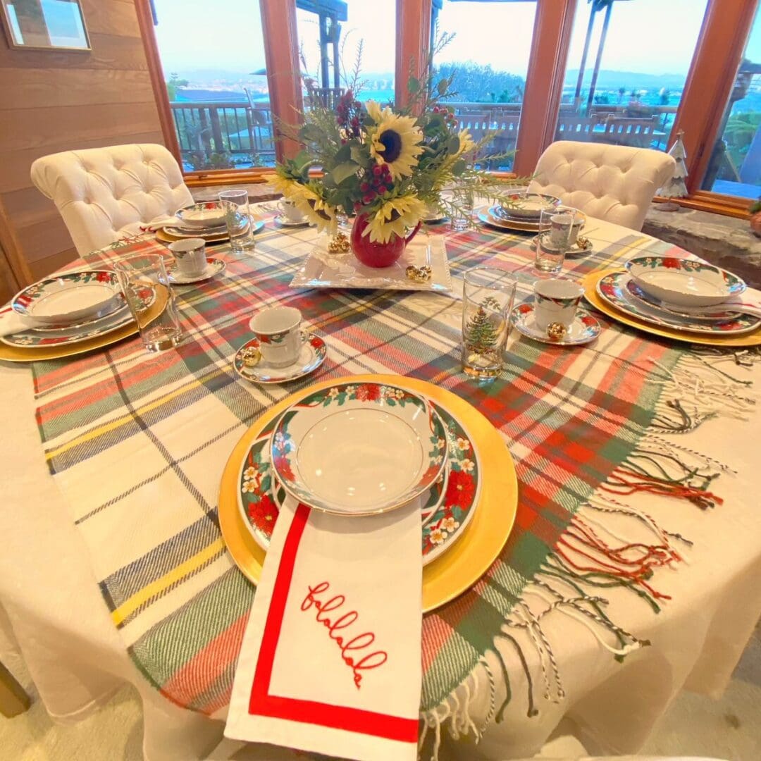 Round holiday table set with a plaid runner, poinsettia china on gold chargers, a falalala napkin and a sunflower centerpiece, tablescape by Simply Luxe