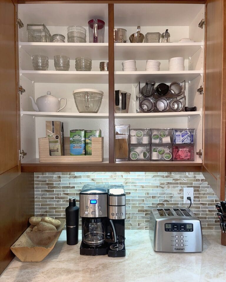 Coffee station after organizing, with glassware, mugs, teapot and coffee pods sorted on white cabinet shelves above the coffee maker, Orange County