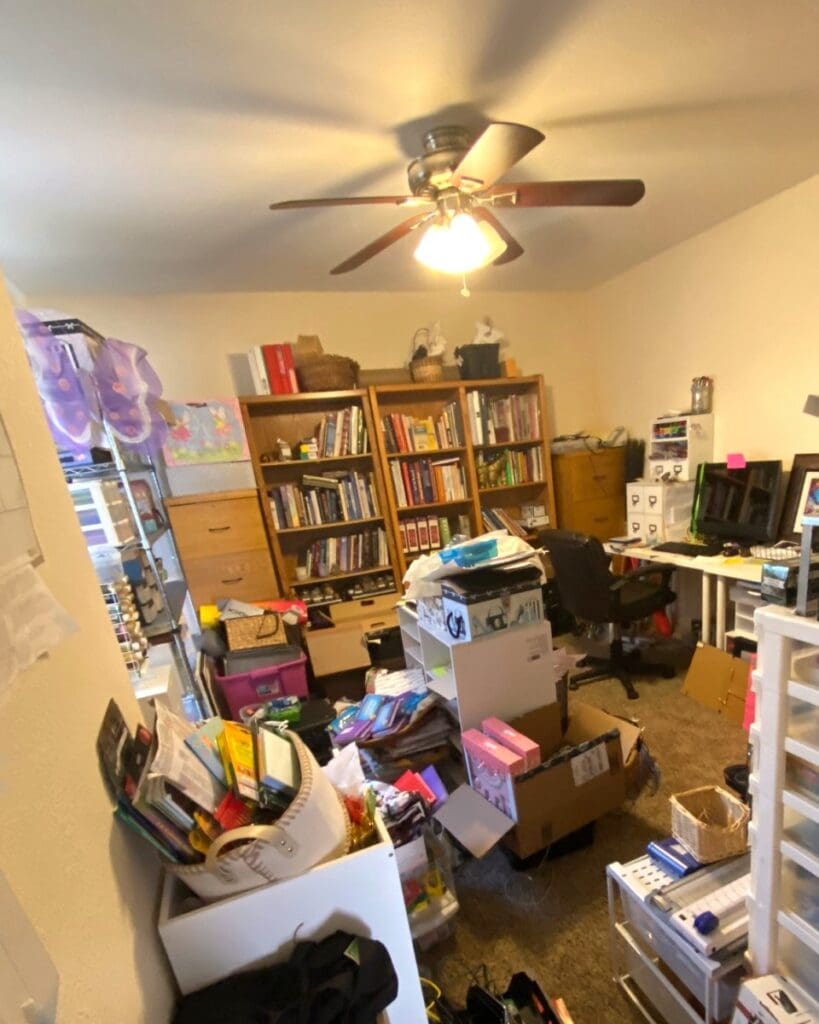 Craft room and home office before organizing, with boxes, bags and supplies piled across the floor