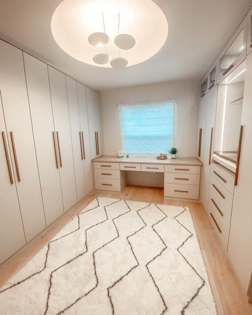 Hannah Godwin's finished celebrity closet and office in La Jolla with linen wardrobes, a vanity desk under the window and a patterned rug, built by California Closets and organized by Simply Luxe
