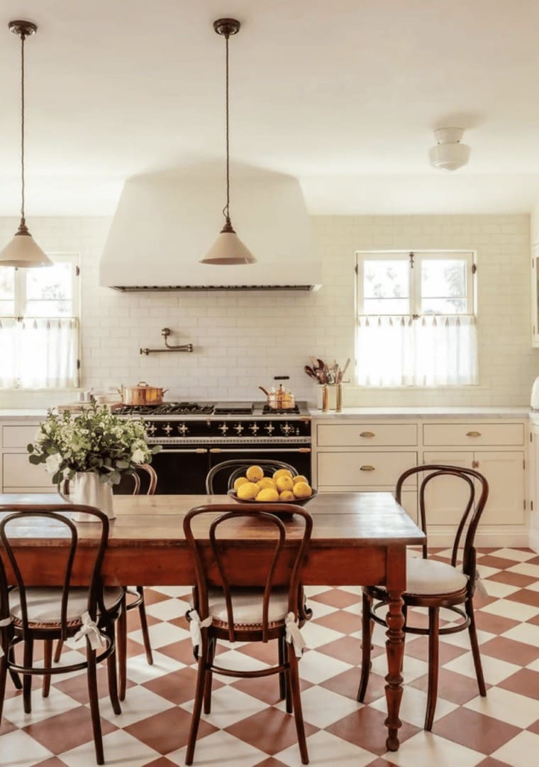Styled kitchen and dining area with wooden table, bentwood chairs, black range, and terracotta checkered floor by Simply Luxe