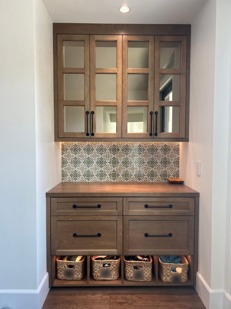 Built-in entryway drop zone with a woven basket for each family member under glass cabinets, organized in San Diego