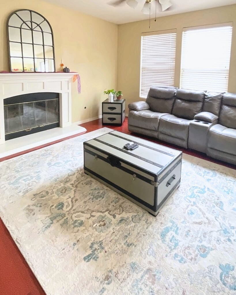 Same family room after Simply Luxe decluttering, with a clear rug, a trunk coffee table and open floor in front of the fireplace