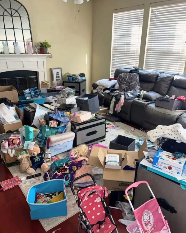 Family room before decluttering, with toys, bags, boxes and a toy stroller covering the floor in front of a leather sectional