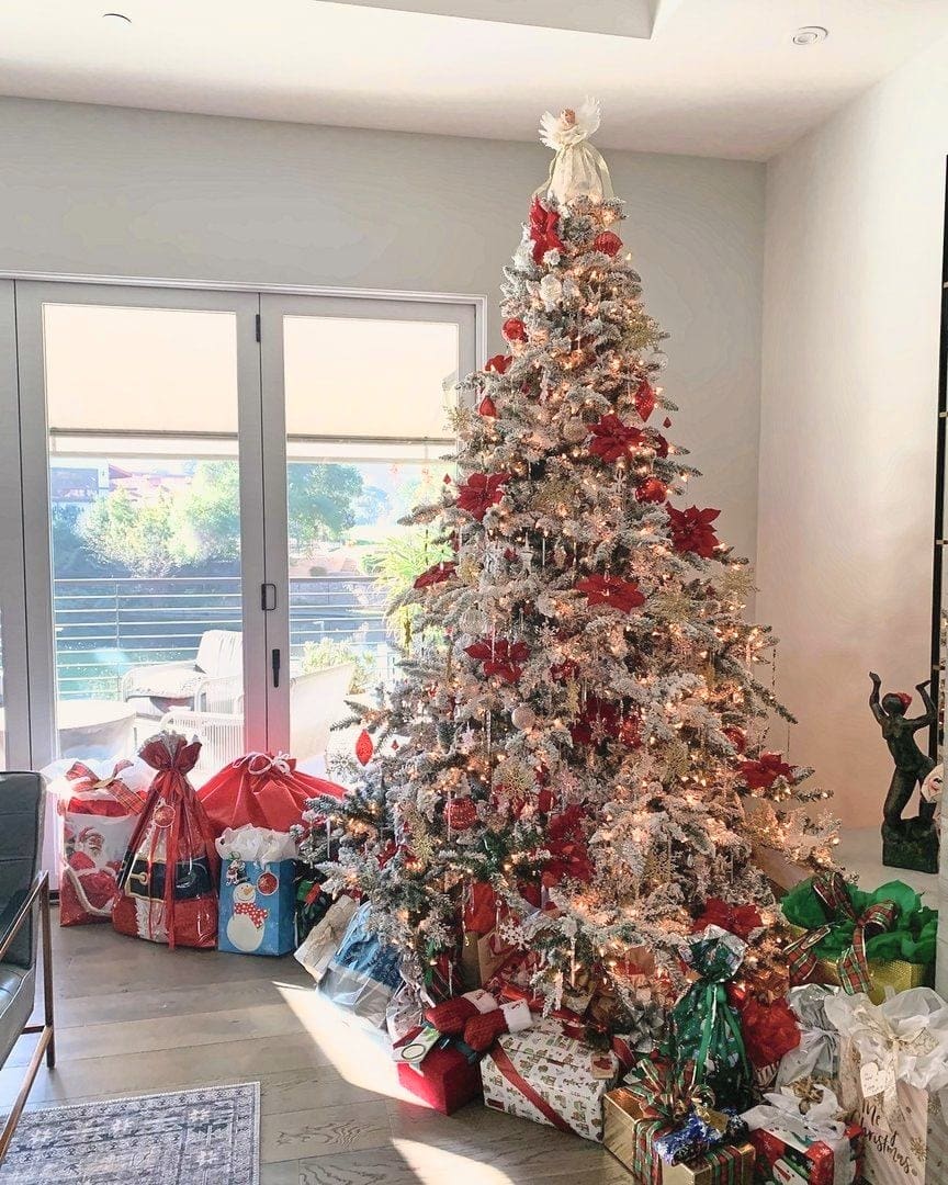 Flocked Christmas tree with red accents and wrapped gifts in a bright living room, holiday decorating by Simply Luxe