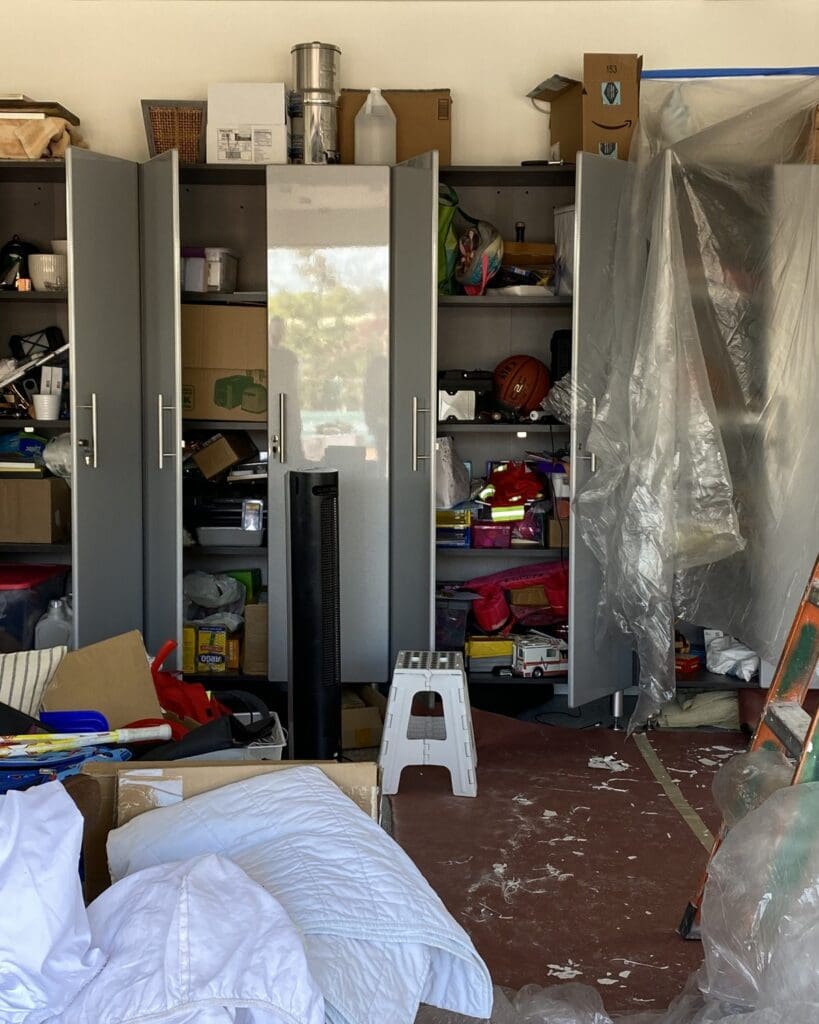 Garage cabinet wall before organizing in Solana Beach, with open cabinets overflowing and bags and a ladder on the floor