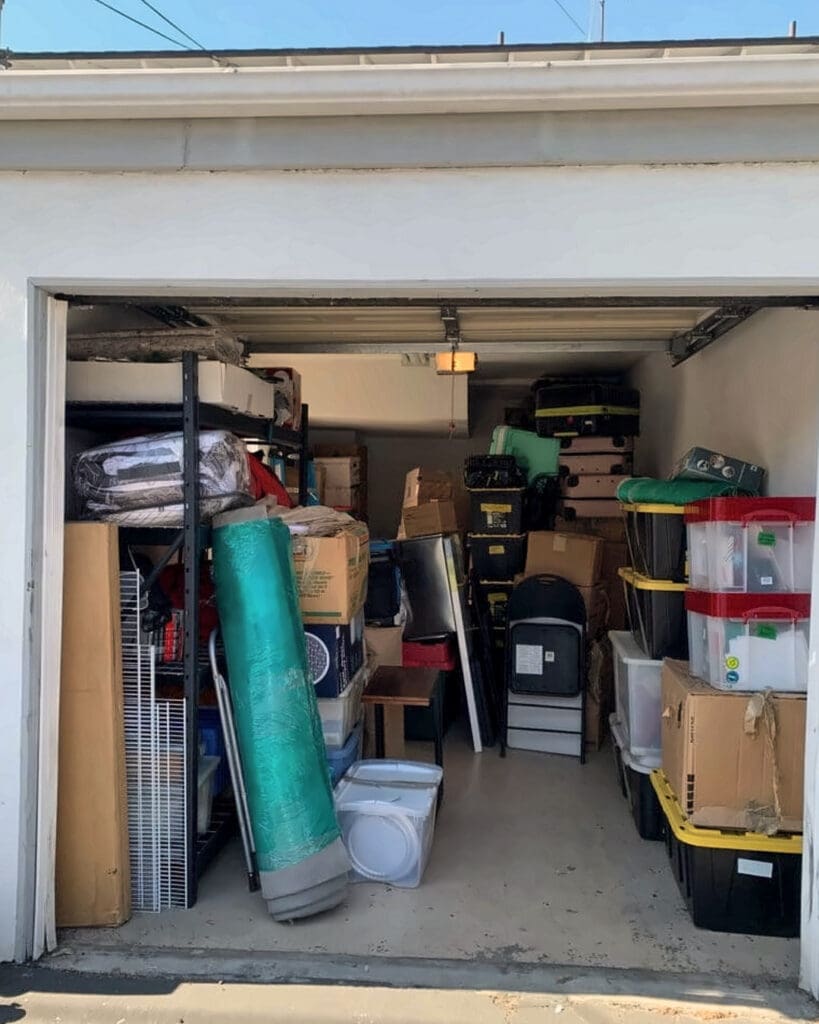 Garage before decluttering, packed wall to wall with boxes, bins, a rolled rug and stacked household items
