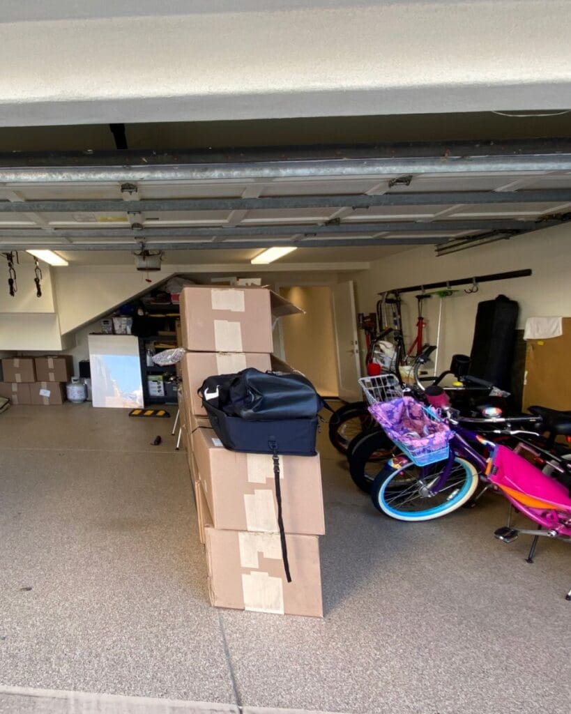 Two car garage before organizing, with stacked moving boxes, bikes and loose gear across the floor