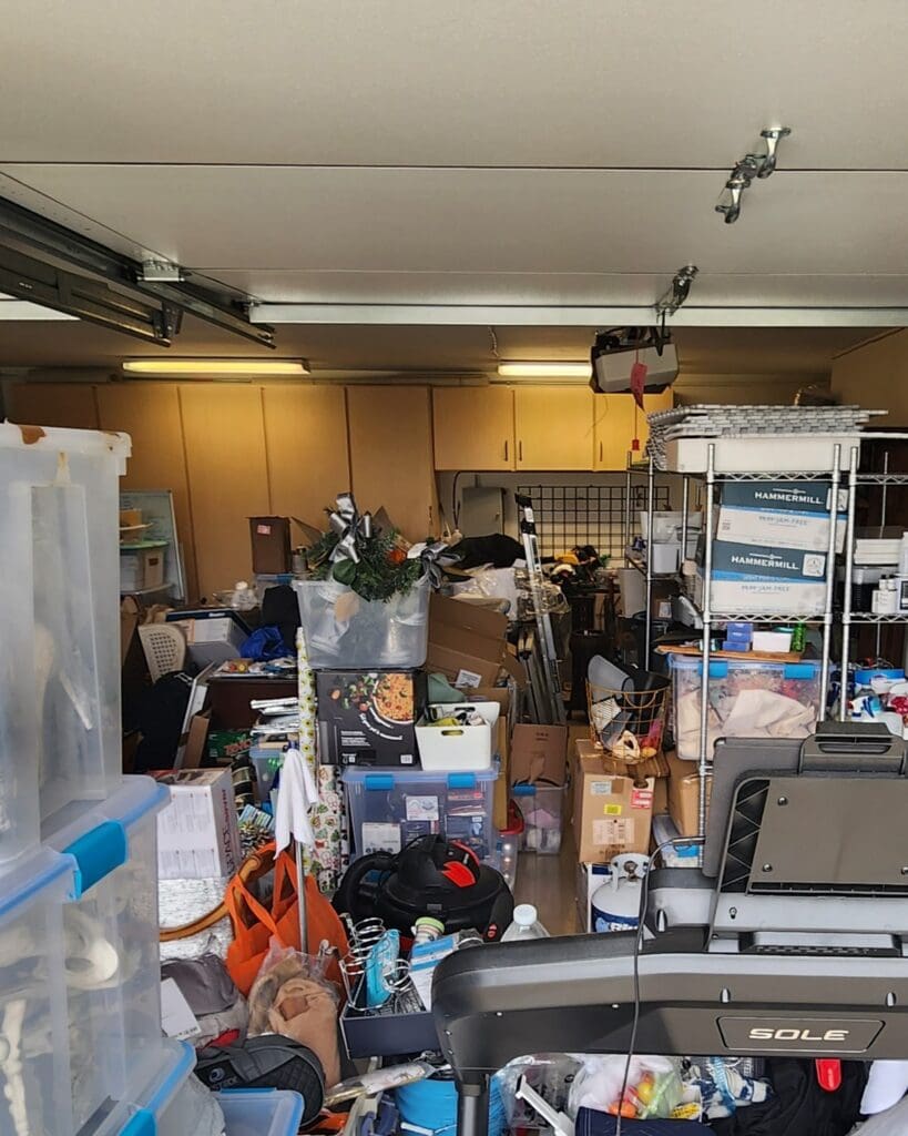 Two car garage before organizing in Carlsbad, packed with stacked bins, a treadmill, boxes and shelving from front to back