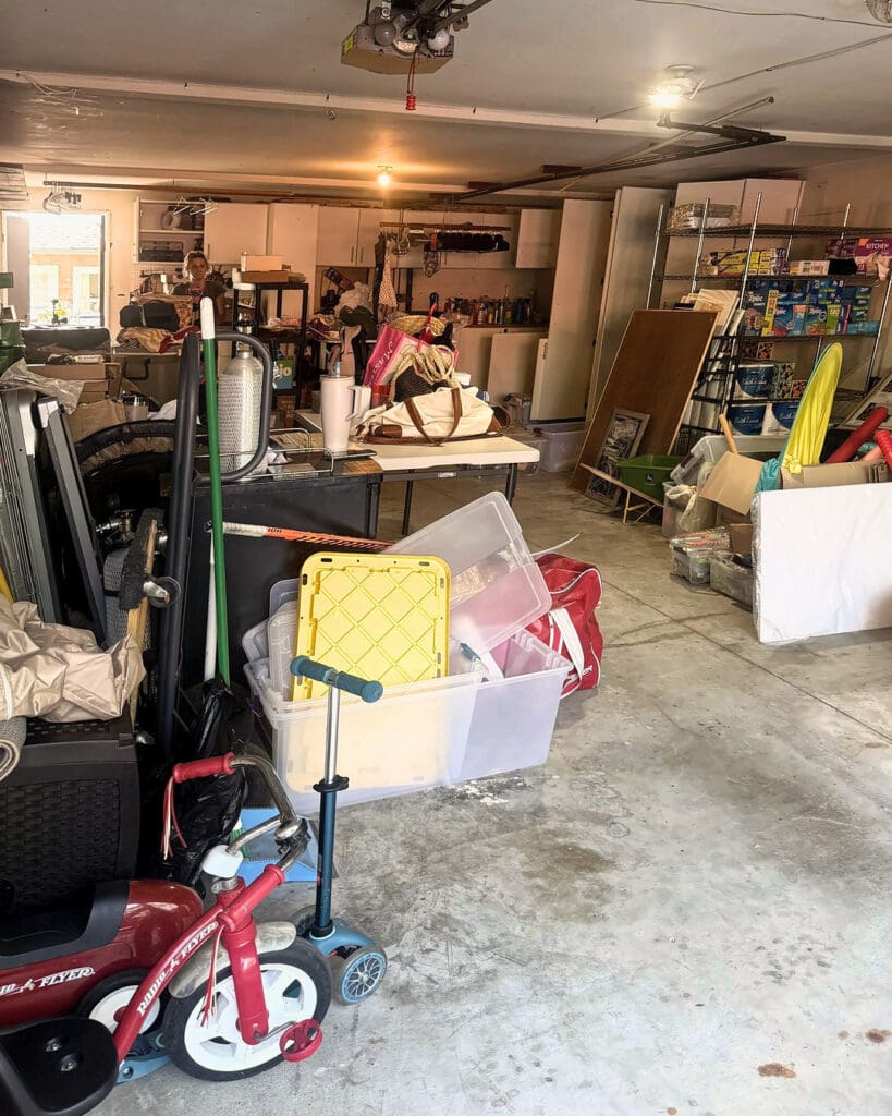 Two car garage before organizing, with ride-on toys, bins, a tricycle and loose gear spread across the floor, Laguna Beach home