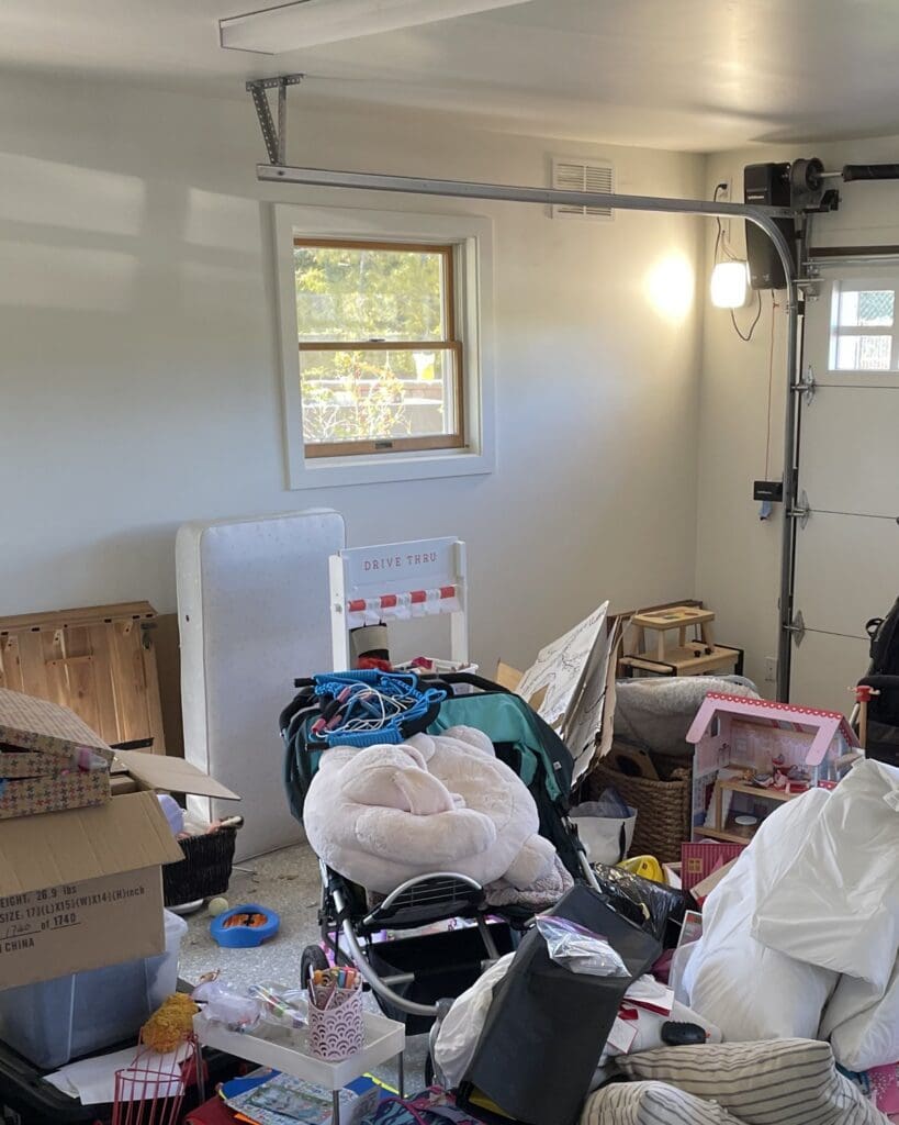 Garage before organizing in Solana Beach, with boxes, a stroller, bags and toys piled under the window