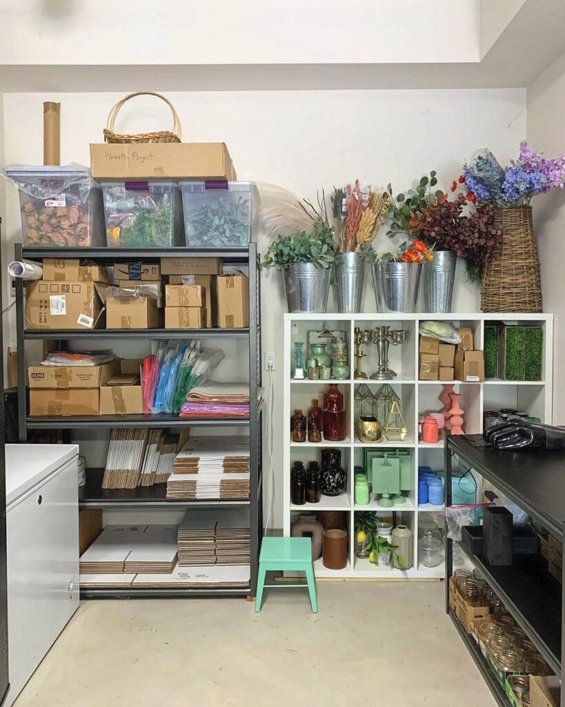 Same garage shelves after Simply Luxe organizing, with bins and boxes lined up, floral stems in buckets and a clear walkway, San Diego